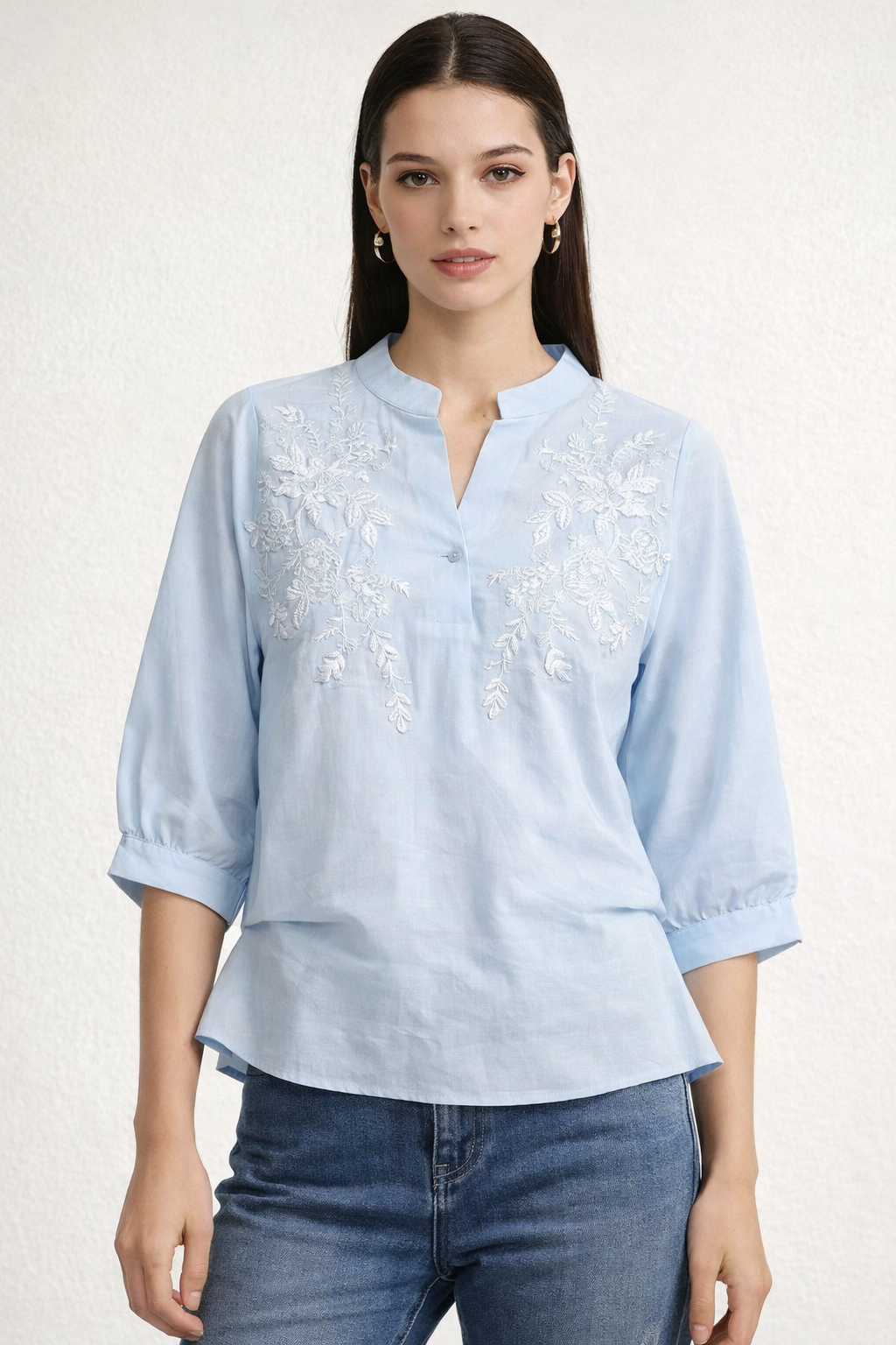 Woman wearing a light blue embroidered blouse with rolled-up sleeves on a white background