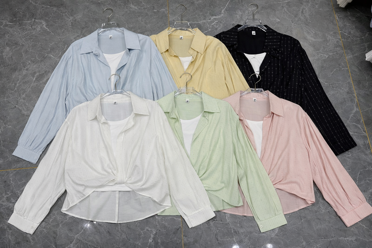 Set of pastel-colored shirts on hangers against a gray background