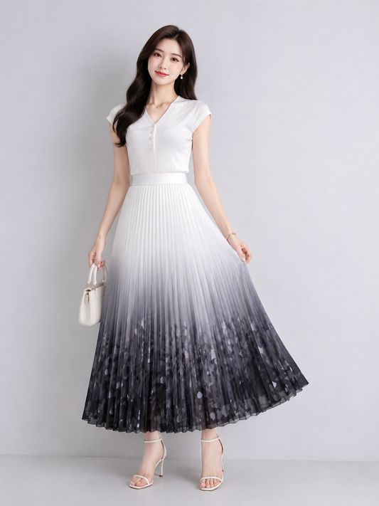 A woman models a sleeveless pleated maxi dress with a white-to-black ombre gradient design, paired with a matching waist belt and holding a small white handbag against a light gray studio background.