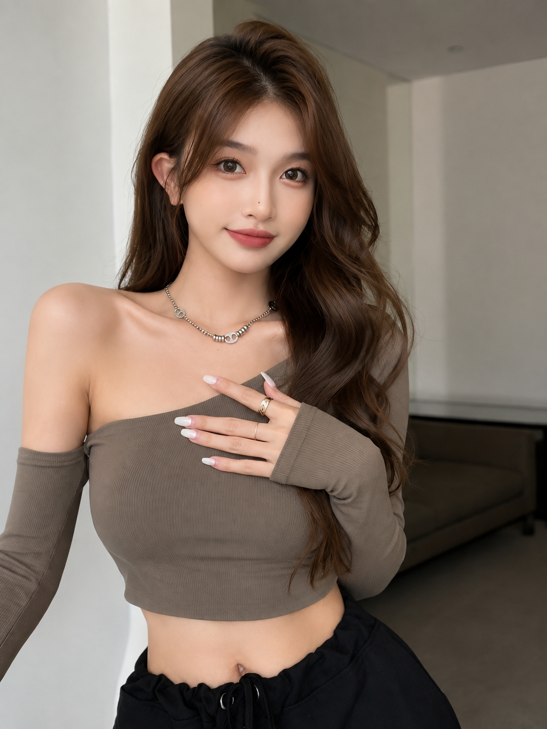 A woman wearing a taupe-brown one-shoulder long-sleeve crop top and black pants, posing indoors.