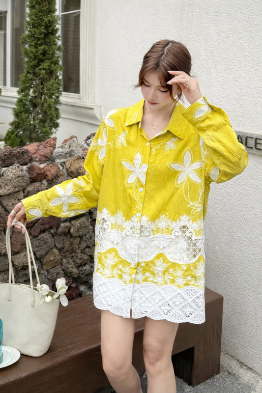 Woman wearing a yellow floral dress standing outdoors near a stone wall.