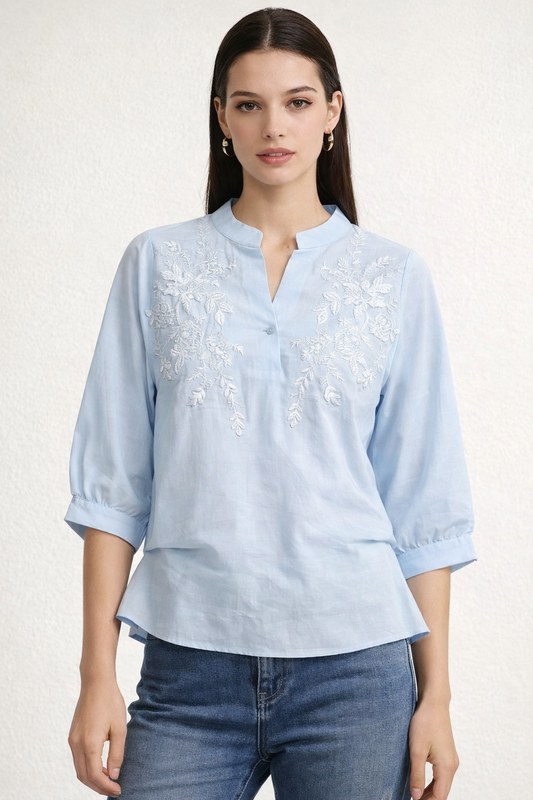 Woman wearing a light blue embroidered blouse with rolled-up sleeves on a white background