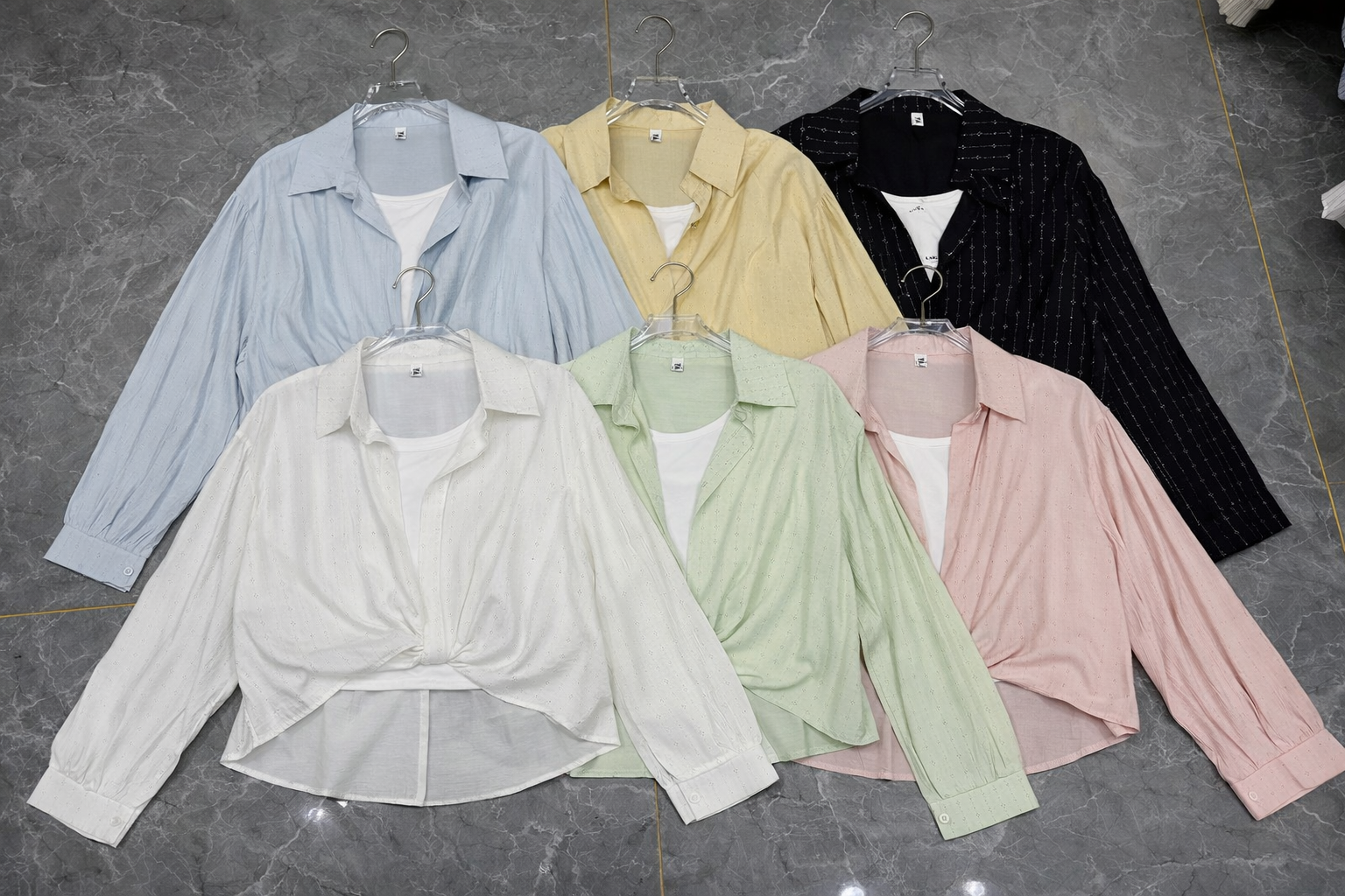 Set of pastel-colored shirts on hangers against a gray background