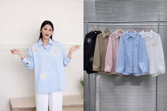 Woman wearing a light blue shirt with floral embroidery, standing next to a rack of similar shirts.