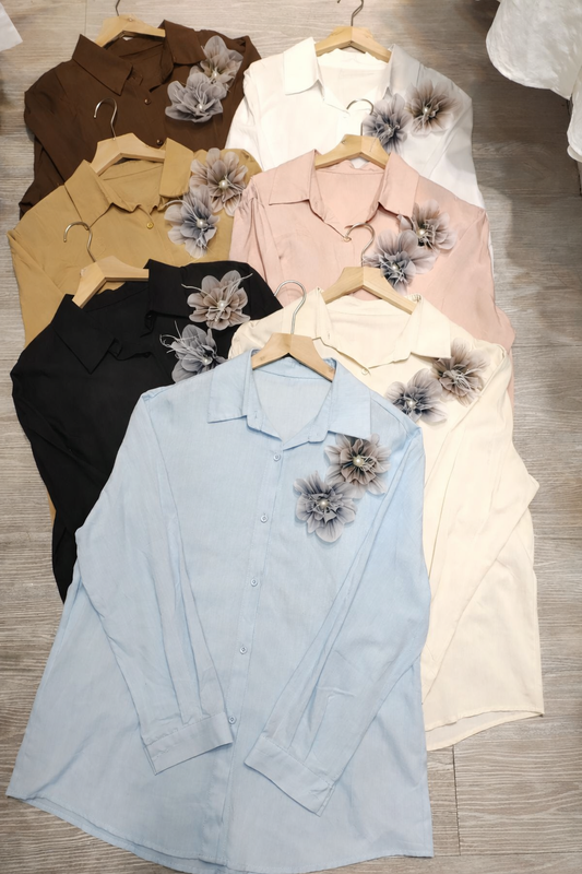 Collection of button-up shirts in various colors with floral accessories on a wooden surface