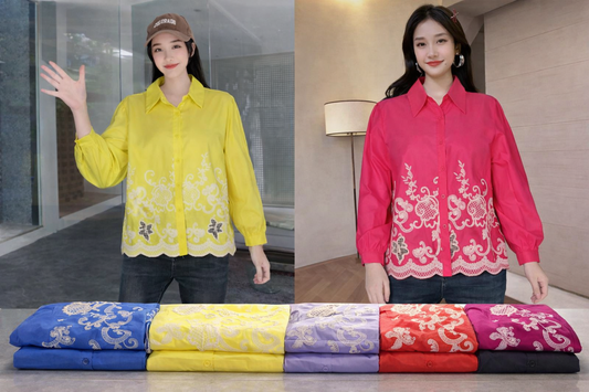 Two women wearing embroidered shirts with a display of folded fabric in various colors.