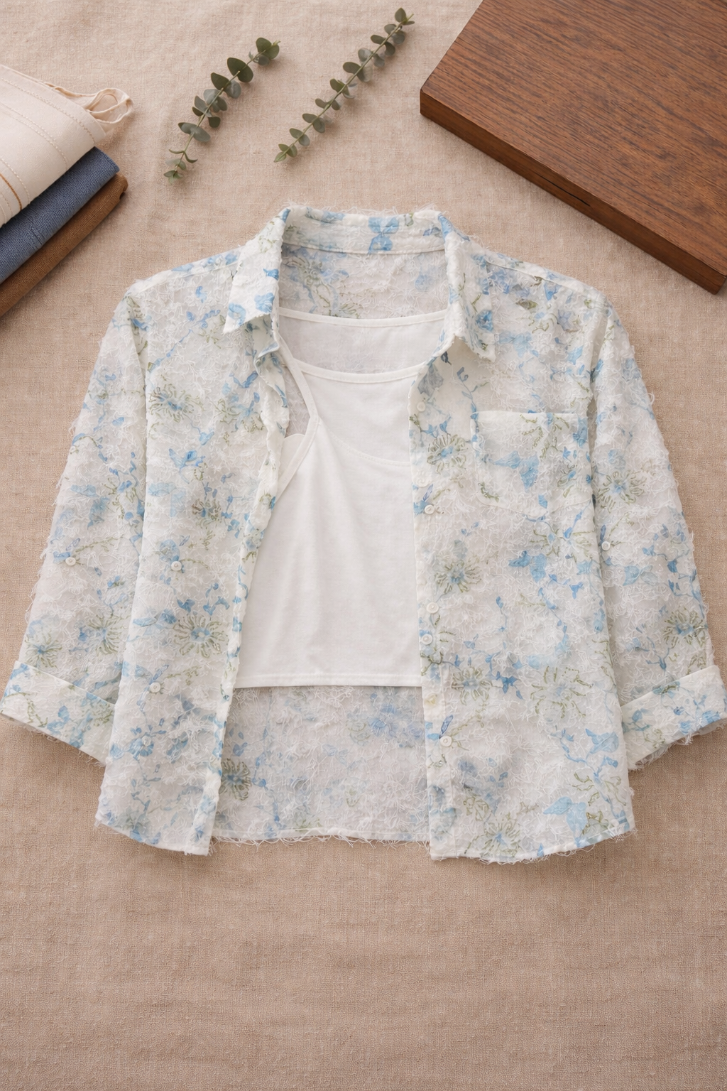 Floral jacket over a white shirt on a beige surface with a wooden block and eucalyptus leaves.